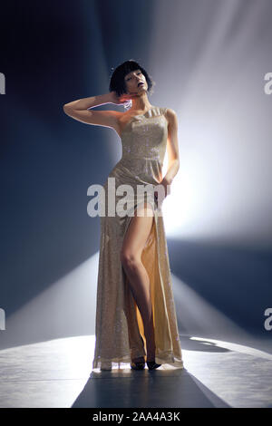 Fashion model in long dress with deep cut on the stage under key light Stock Photo