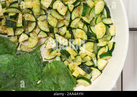 Zucchini and spinach. Roasted sliced zucchini and spinach with some seasoning on a frying pan close up, view from above Stock Photo