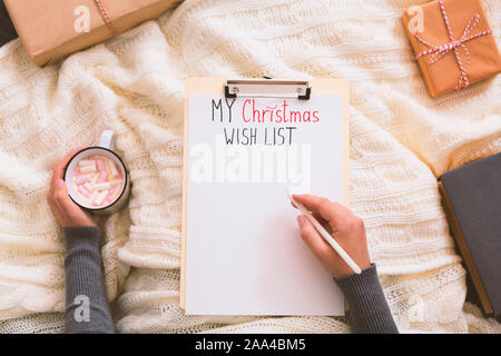 Woman writing with pen on clipboard and drinking hot cocoa Stock Photo