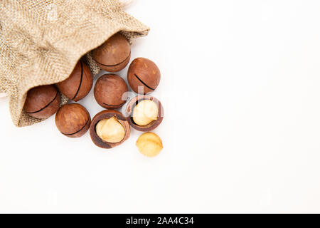 Pile macadamia nuts open kernels and shells in burlap bag on white background, top view. Stock Photo