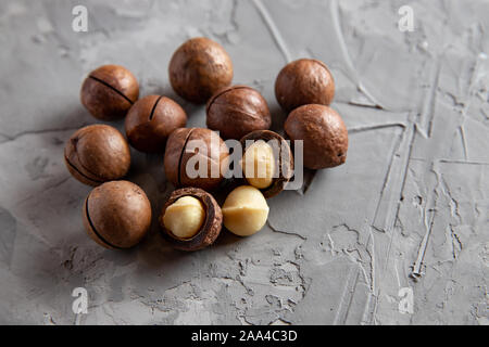 Pile macadamia nuts open kernels and shells on gray concrete background, top view. Stock Photo