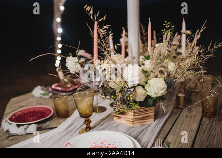 Romantic dinner on a wooden table with burgundy plates and fresh flowers.  Stock Photo