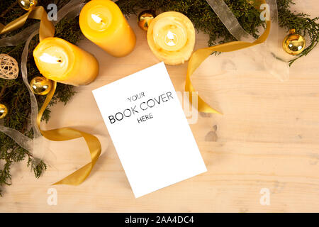 Christmas flat lay for a book presentation: book with blank cover settled with three lit candles , white organza and gold satin ribbons, gold baubles Stock Photo