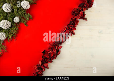Flat lay red Christmas copy space with a diagonal red stripe on light wooden background, pine branches, white pine cones and red petals Stock Photo