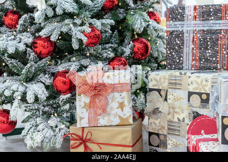 Gift boxes near a snow-covered Christmas tree with red balls. Stock Photo