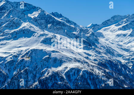 A rescue helicopter in the high mountains. Tall Alps surrounding the vehicle that is getting ready to land. Mountains slopes are covered with thick sn Stock Photo