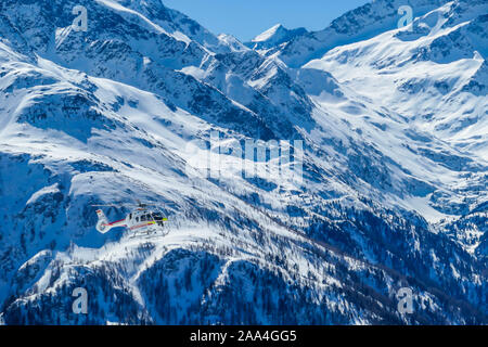 A rescue helicopter in the high mountains. Tall Alps surrounding the vehicle that is getting ready to land. Mountains slopes are covered with thick sn Stock Photo