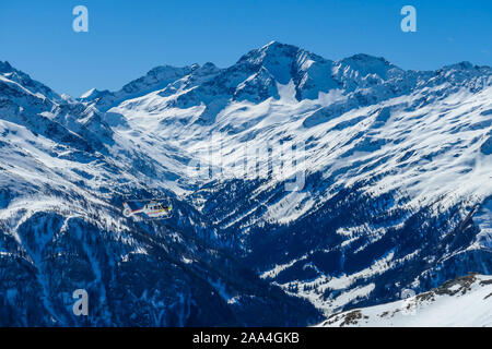 A rescue helicopter in the high mountains. Tall Alps surrounding the vehicle that is getting ready to land. Mountains slopes are covered with thick sn Stock Photo