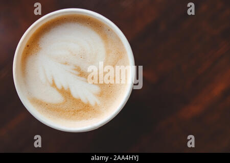 Top view texture of foam and coffee cappuccino latte bubbles in paper cup on wooden table, lens flare. Stock Photo