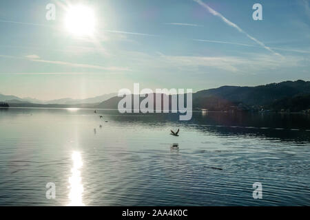 A view on a lake and Alps in the back. The calm surface of the lake is reflecting the mountains, sunbeams and clouds. Clear and sunny day. Calm and re Stock Photo