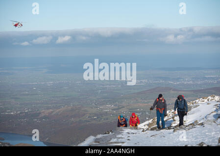 Snowdon Summit, Gwynedd, Wales, UK. 10th November 2019. A HM Coastguard Rescue helicopter patrols the skies above a snow-capped Snowdon in Wales. Stock Photo