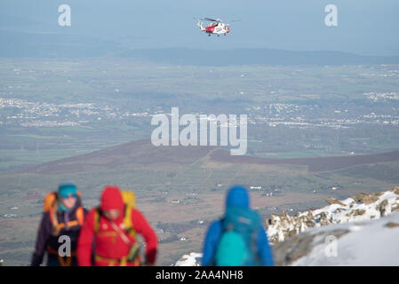 Snowdon Summit, Gwynedd, Wales, UK. 10th November 2019. A HM Coastguard Rescue helicopter patrols the skies above a snow-capped Snowdon in Wales. Stock Photo