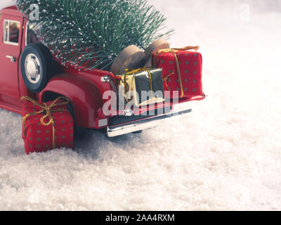 Red Christmas truck with Christmas trees and gift boxes in the snow, selective focus on the foreground, space for your text on the right side Stock Photo