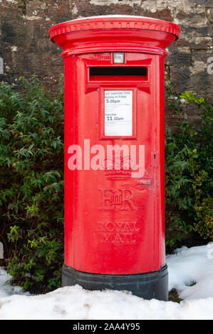 A traditional red British Post Box in a snowy rural setting. An old fashioned pillar box with snow on the ground. Stock Photo