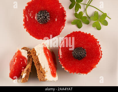Top view and close-up of two homemade cheesecakes bathed in strawberry sauce and accompanied by another halved cheesecake and clover leaves on white b Stock Photo