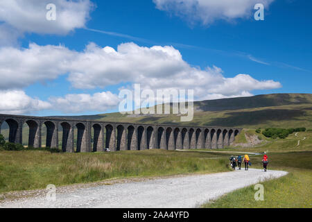 Walkers heading along track towards Ribblehead Viaduct and Whernside, one of the Three Peaks in the Yorkshire Dales National Park, UK. Stock Photo