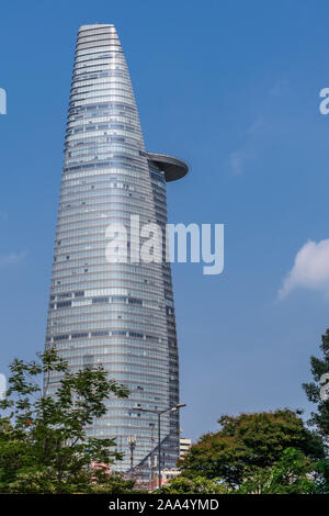 Ho Chi Minh City, Vietnam - March 12, 2019: Downtown street scenery. Bitexco financial tower against blue sky with green foliage at foot. Stock Photo