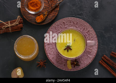 Cup of ayurvedic golden turmeric latte milk with curcuma powder, cinnamon, ginger and anise star on dark background, Top view Stock Photo