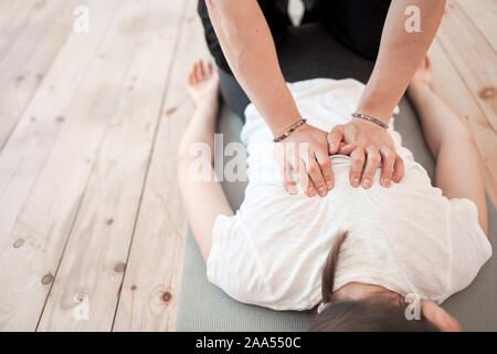 Man does woman's back massage in white T-shirt lying on gray rug in gym Stock Photo
