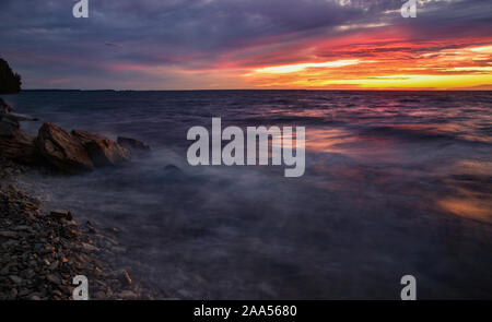 Beautiful sunset over Green Bay with water swirling in motion, streaking over rocks and splashing along shoreline near Ellison Bay, Wisconsin, USA Stock Photo