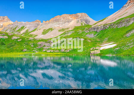 Landscape view of green grass meadow and Ice lake water reflection near Silverton, Colorado in August 2019 summer on summit with snow Stock Photo