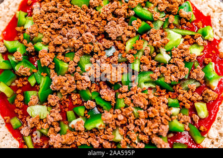 Macro flat top closeup of homemade uncooked pizza with tomato sauce and toppings green bell peppers chopped with ground vegan beef crumbles Stock Photo