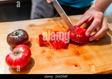 Hands of man chopping vegetables on cutting board table in kitchen with juicy red and black heirloom tomatoes with vibrant color from garden Stock Photo