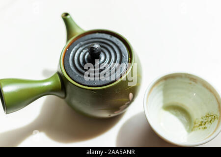 Cast iron and green clay teapot on table closeup with empty used cup of Japanese drink with kyusu handle brewing during ceremony Stock Photo