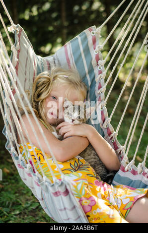 lovely girl in hammock having good time with cute cat in beautiful sunny summer day Stock Photo