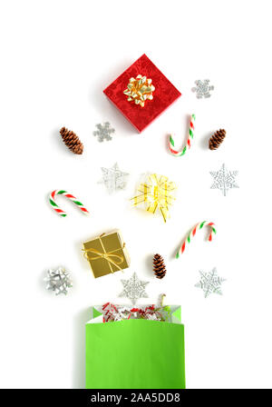 A variety of Christmas objects spilling from green bag in flat lay composition.  In vertical format on white background. Christmas concept. Stock Photo