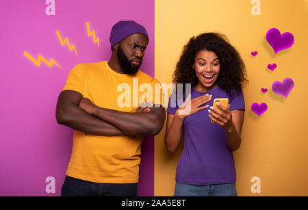 Girl receive a lot of hearths on social and boy is jealous about it. Yellow and violet background Stock Photo