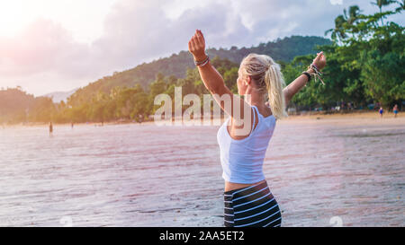 Happy blond beautiful women raising her hands on Ao Nang beach at sunset, Krabi Thailand Stock Photo