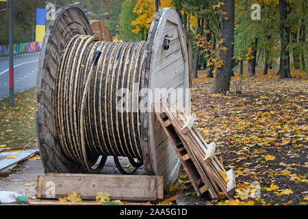 In the park against the background of autumn yellow leaves there is a drum with cable, close-up. Power cable for laying in the trench on the drum, nex Stock Photo