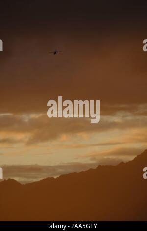 Bush plane flying under a dramatic sunset landscape in the Knik River Valley, Chugach Mountains, Alaska Stock Photo