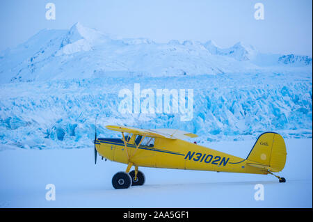 A Cessna 120 bush plane parked on snow covered, frozen Inner Lake George, in front of Colony Glacier, Chugach Mountains, Alaska Stock Photo