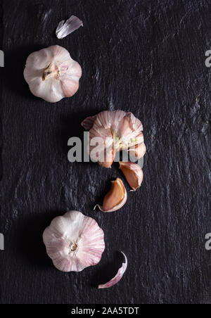 Overhead view of three bulbs of raw purple garlic on a black surface Stock Photo
