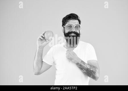 Its always better when its natural. Hipster pointing at natural orange fruit on yellow background. Bearded man with natural vitamin food. Be smart, eat natural. Stock Photo