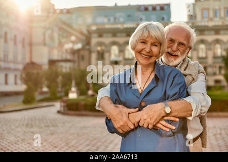 Love has no age limit. Happy senior couple in casual clothing embracing each other and smiling while standing outdoors. Love concept. Family Stock Photo
