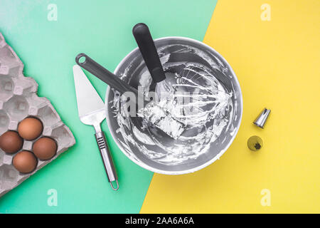 Cake baking making utensils in mixer bowl after cake making, nozzles, raw eggs on flat lay green yellow background Stock Photo