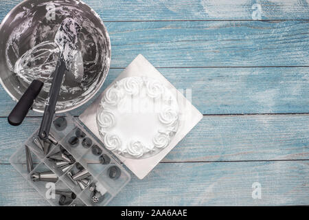 Baking utensils tools in mixer bowl after cake frosting, and a box of nozzles on flat lay rustic blue background Stock Photo