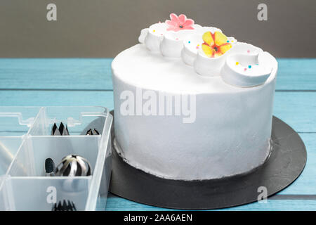 Fresh cream frosted cake and box of piping nozzles on blue rustic table Stock Photo