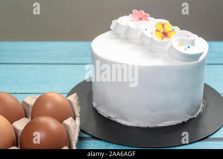 Fresh white cream frost cake and raw eggs on blue rustic table, isolated Stock Photo