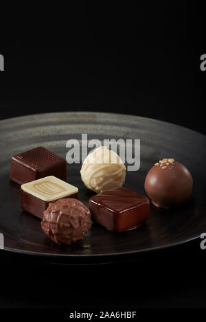 Title: A pile of exquisitely beautiful chocolate cubes placed on a dark grey ceramic plate with a water ripple. Stock Photo