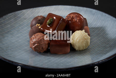A pile of exquisitely beautiful chocolate cubes placed on a dark blue ceramic plate with parallel stripes. Stock Photo