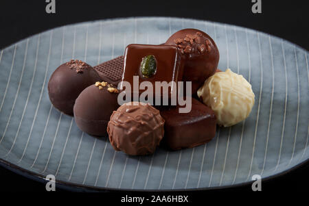 A pile of exquisitely beautiful chocolate cubes placed on a dark blue ceramic plate with parallel stripes. Stock Photo