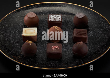 A pile of exquisitely beautiful chocolate cubes placed on a dark gray lined ceramic plate with gold trim Stock Photo