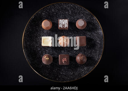 A pile of exquisitely beautiful chocolate cubes placed on a dark gray lined ceramic plate with gold trim Stock Photo