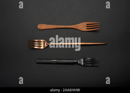 Three different material forks, wooden forks, long handle gold metal forks, black plastic forks Stock Photo