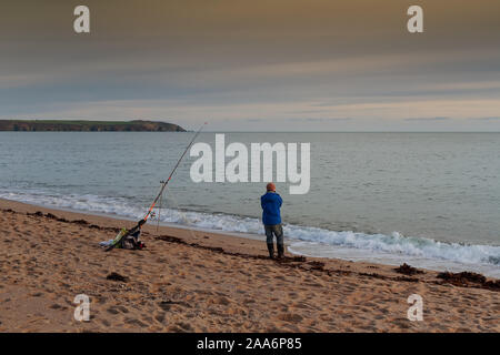 A lonely fisherman is looking at the sea during sunset in St. Austell, Cornwall, United Kingdom. Stock Photo