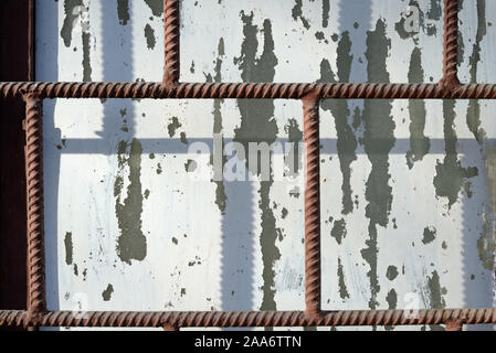Old window painted by white paint behind a rusty brown bars on a sunny day. Abstract background Stock Photo